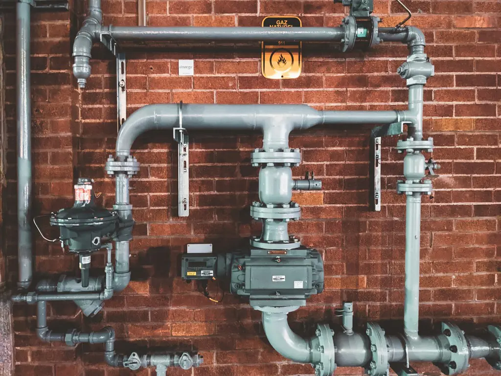 Grey metal supply pipes and valves mounted across a red brick wall.